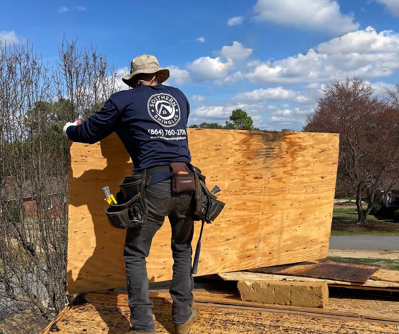 Southern Shingles employee wearing protective gear holding up roof decking to be laid down.